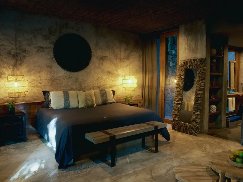 Dimly lit king bed in Signature Suite with textured wall and bedside lamps at BE Destination Tulum