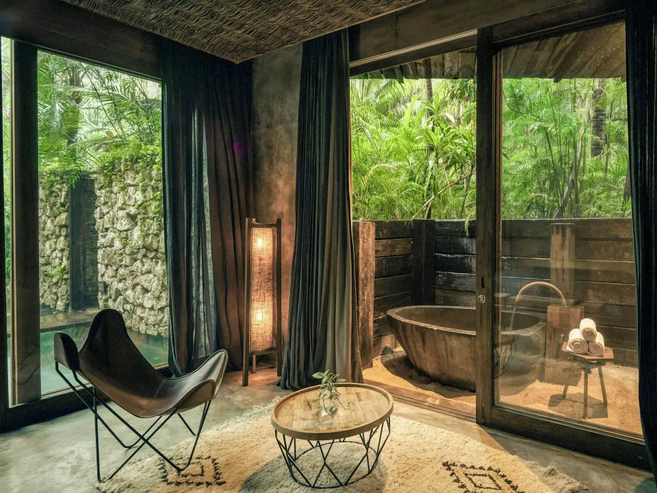 Indoor seating area and outdoor soaking tub visible through glass in Signature Suite at BE Destination Tulum
