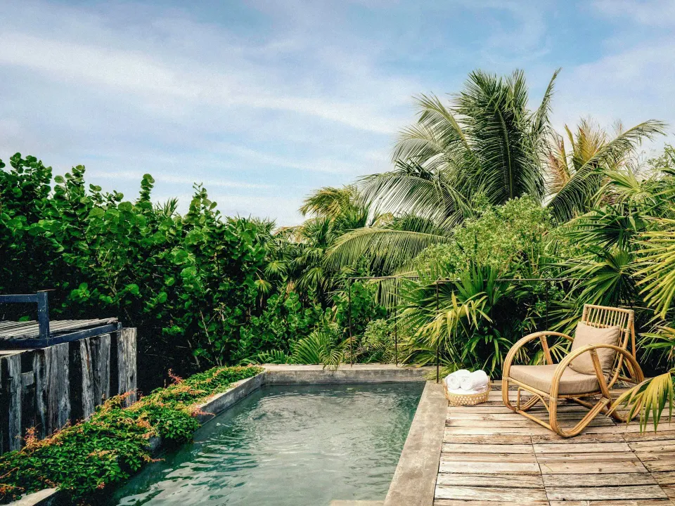 Private plunge pool and wooden deck with chair surrounded by palms at BE Destination Tulum.