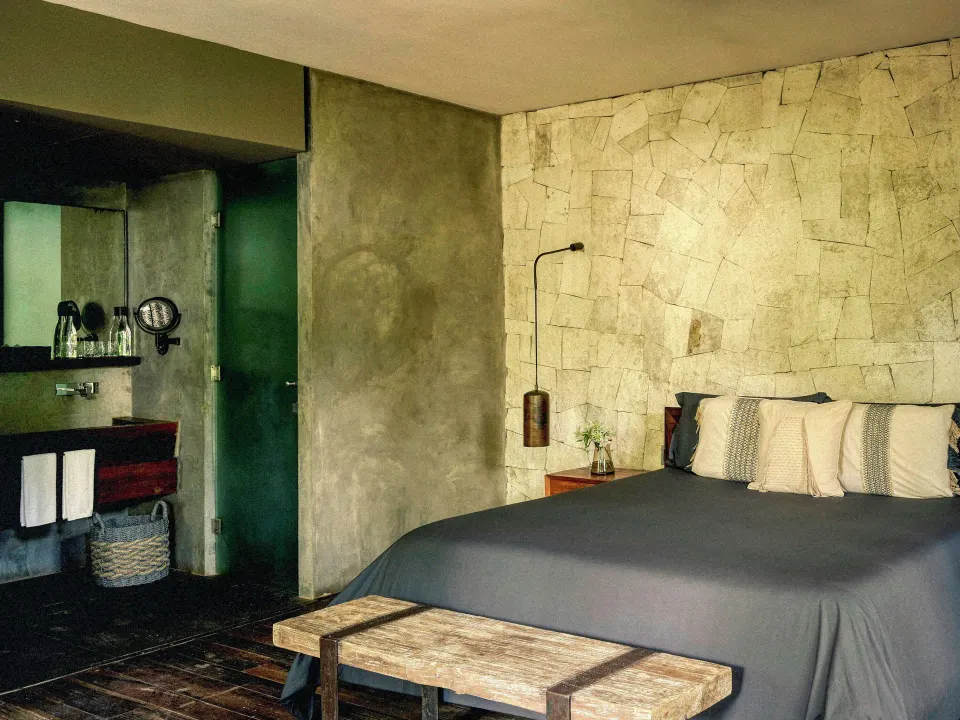 Alcove Suite king bed with stone accent wall and open bathroom at BE Destination Tulum