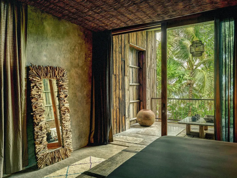 Interior view looking out to the balcony of an oceanfront suite at BE Destination Tulum with rustic mirror