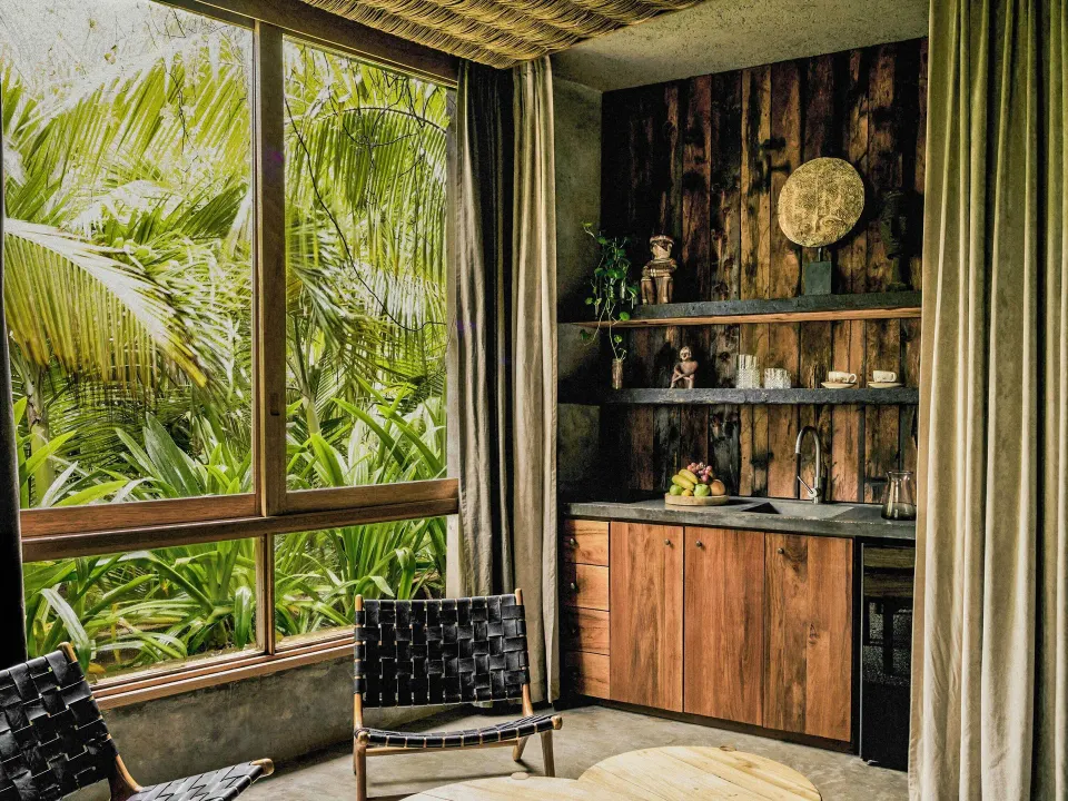 Suite kitchenette and seating area at BE Destination Tulum with wood shelving and a lush window view