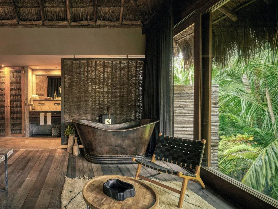 Palm Suite freestanding tub and chair by floor-to-ceiling windows at BE Destination Tulum