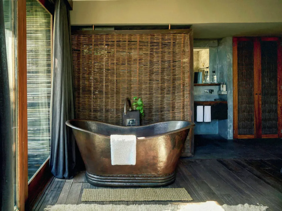 Freestanding copper bathtub in a suite with woven partition at BE Destination Tulum.