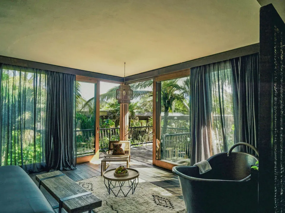 Suite seating area and floor-to-ceiling windows opening onto a private balcony at BE Destination Tulum.
