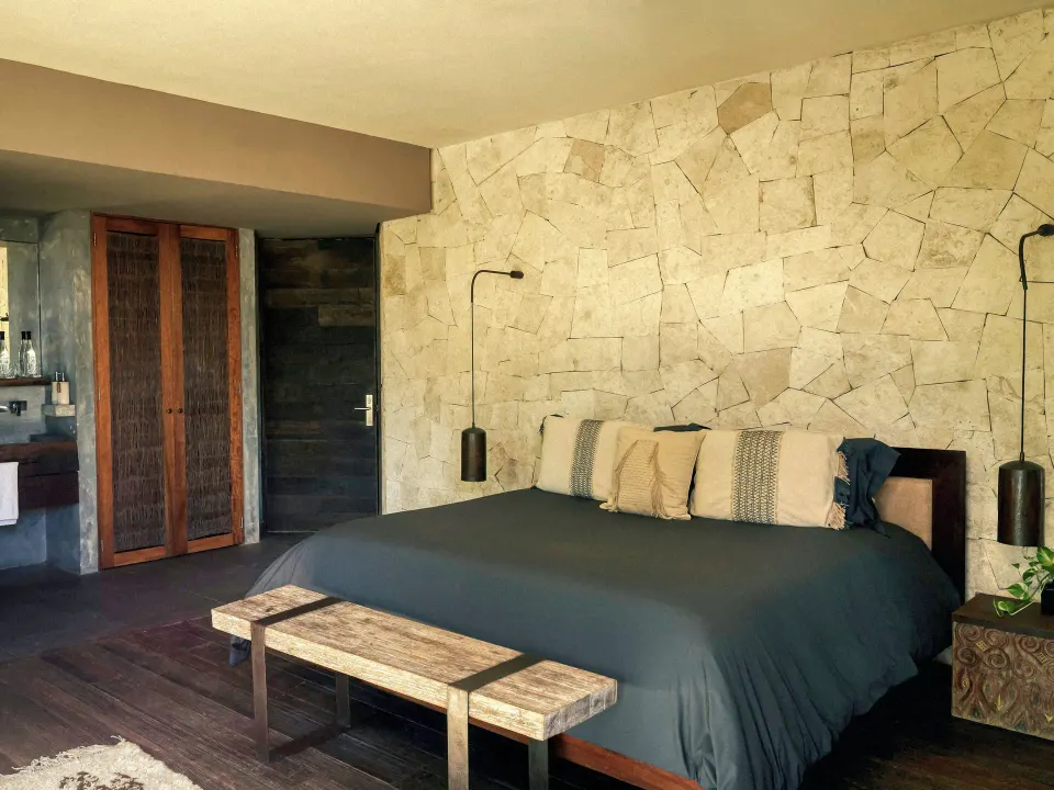 Bedroom suite with king bed and textured stone wall at BE Destination Tulum.