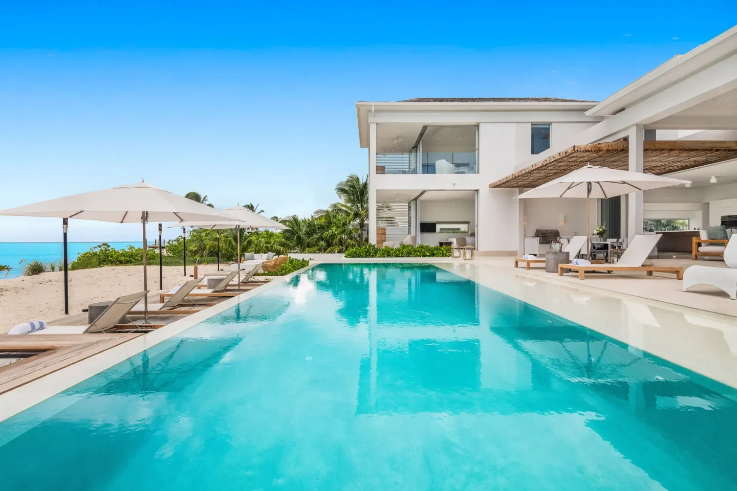 Beachfront pool with loungers, umbrellas, and villa exterior at Beach Enclave.