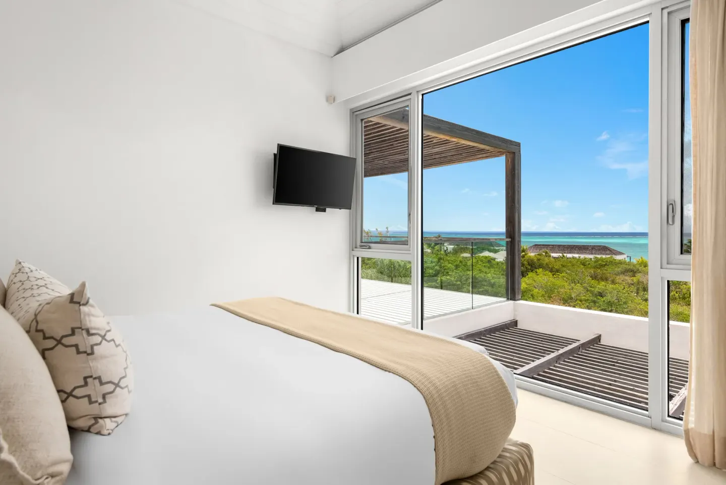 Bedroom with bed, wall TV, and balcony view over turquoise water at Beach Enclave.