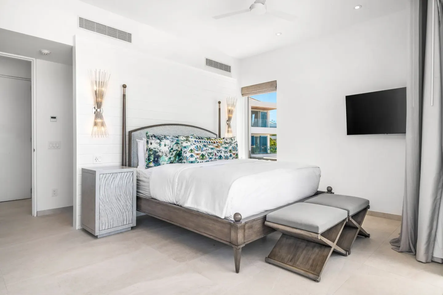King bed guest room with wall-mounted TV and bench at Beach Enclave.