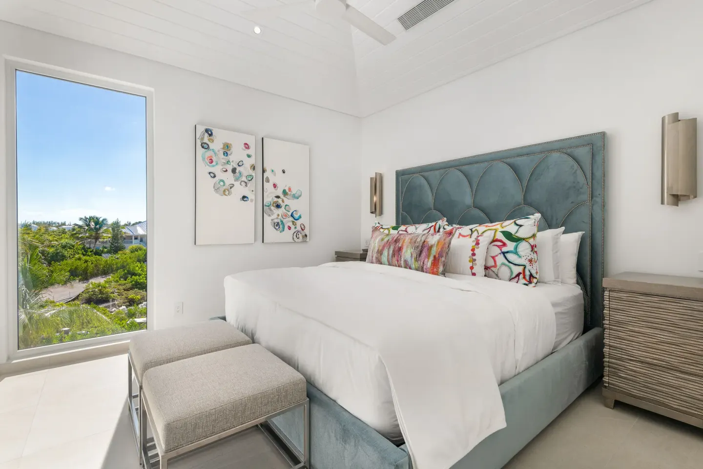 King bed guest room with blue headboard and garden view window at Beach Enclave.