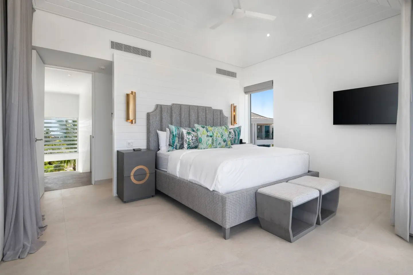 King bed guest room with wall-mounted TV and balcony doorway at Beach Enclave.