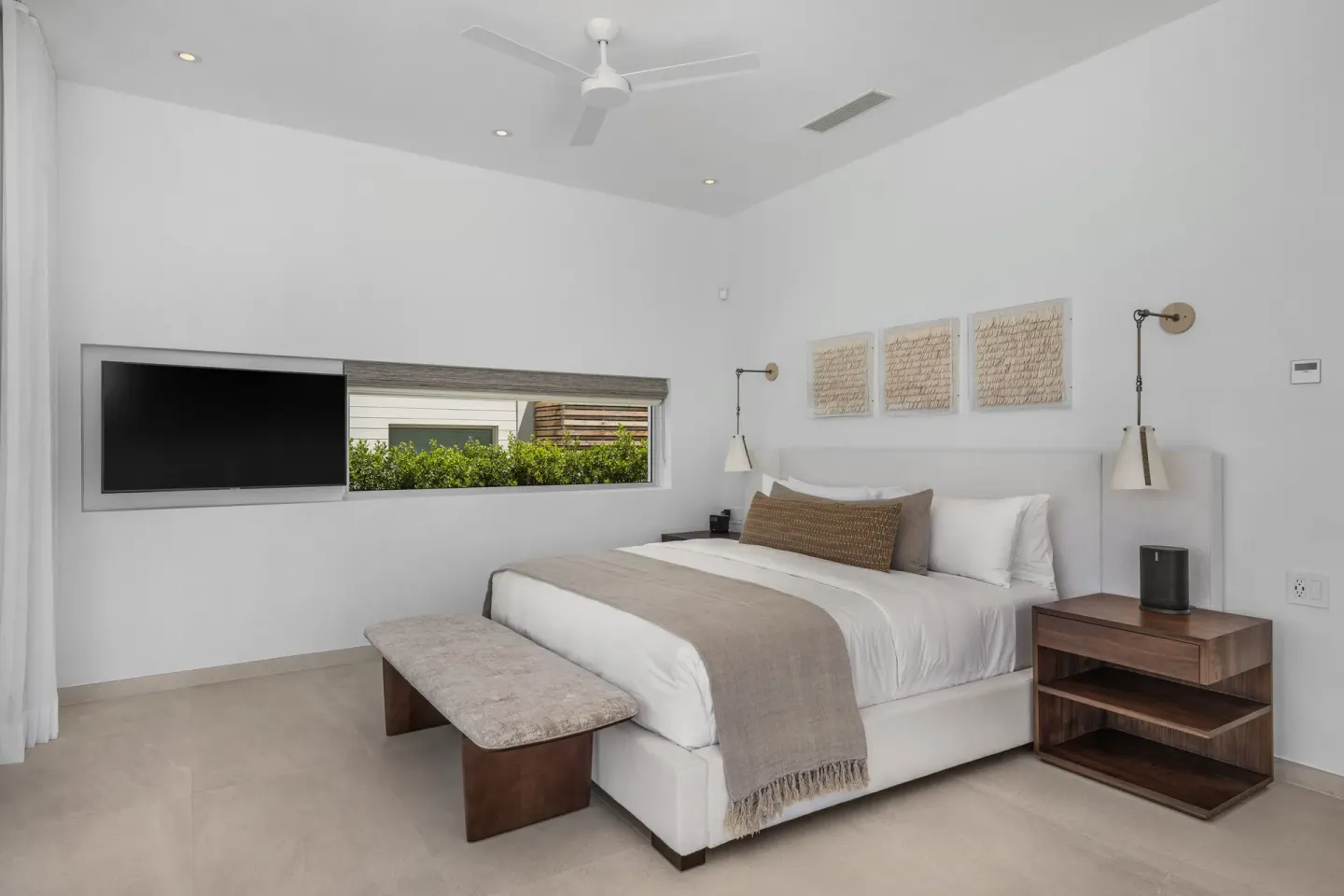 Minimal king bedroom with wall-mounted TV and bench at Beach Enclave.