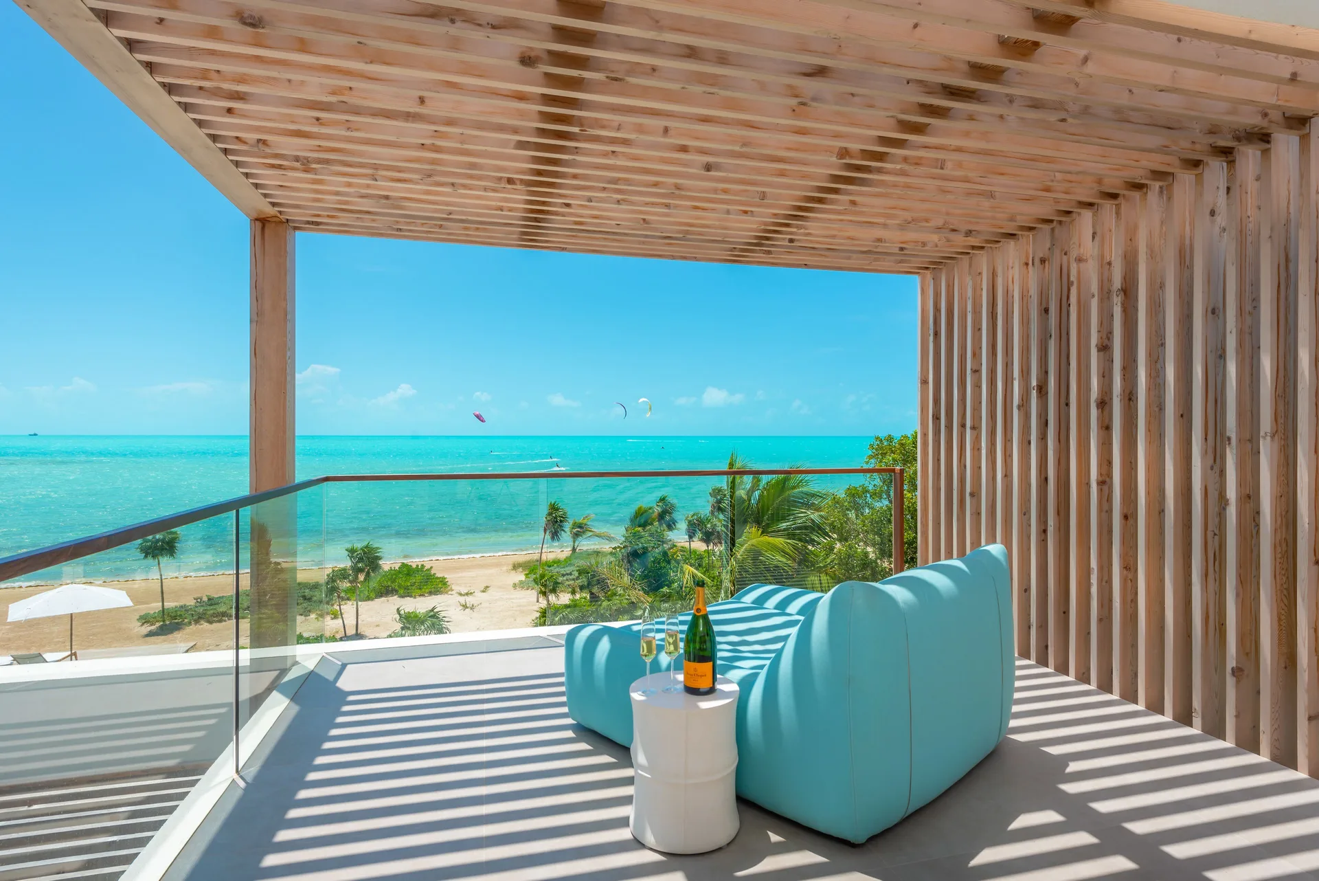 Covered ocean-view terrace with blue sofa and glass railing at Beach Enclave.