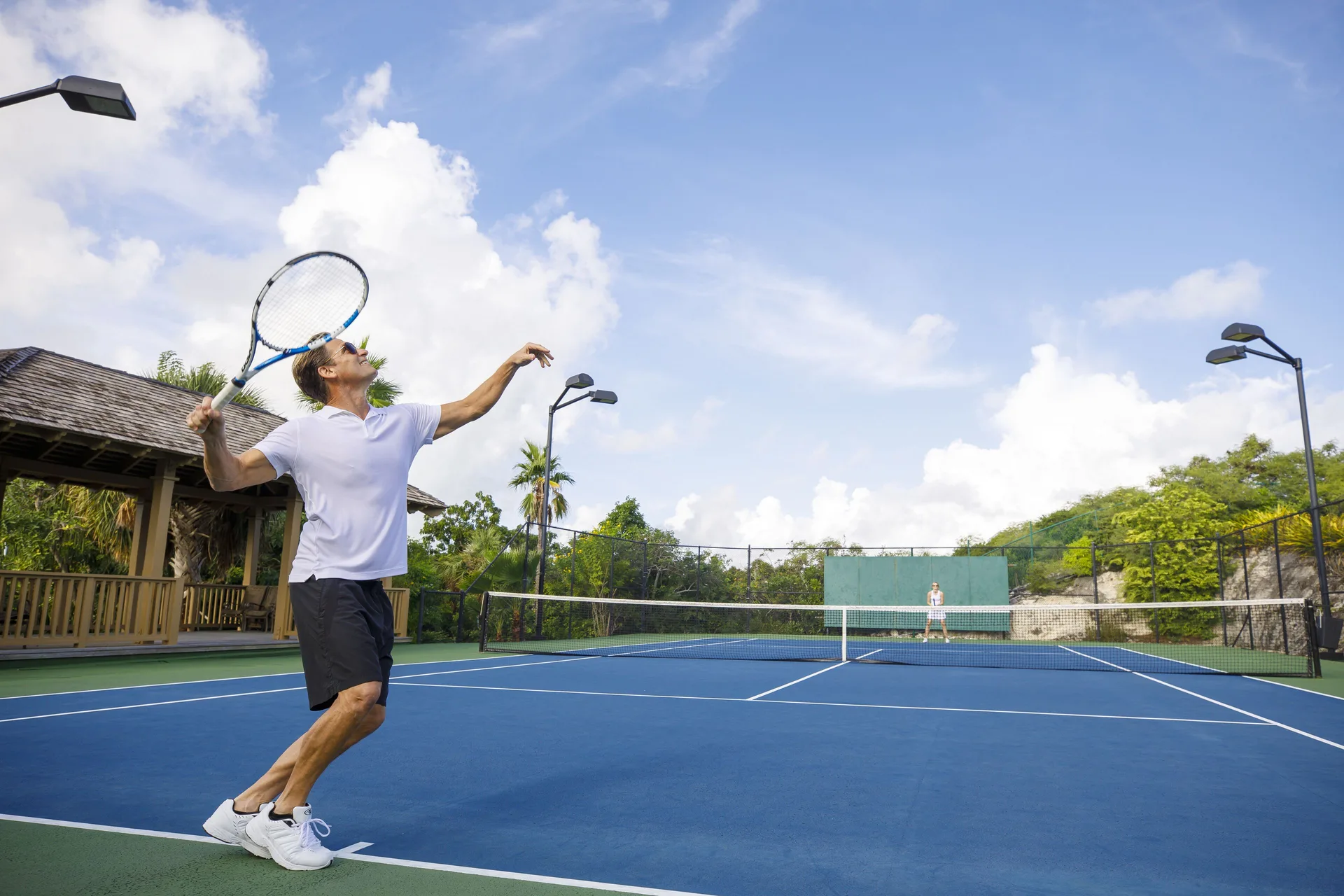 A guest serves on an outdoor tennis court at Beach Enclave.
