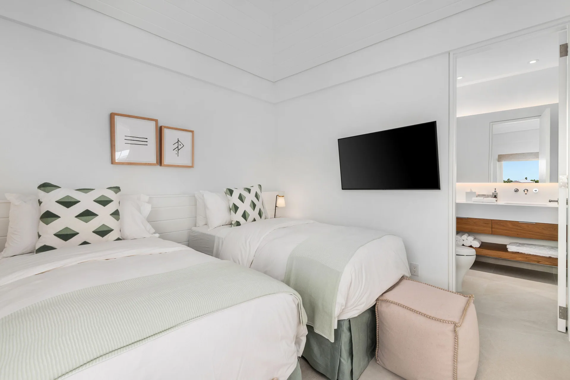 Twin bedroom with an open bathroom doorway and wall-mounted TV at Beach Enclave.