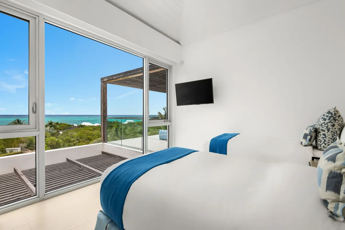 White bedroom with blue bed accents and ocean-facing windows at Beach Enclave.