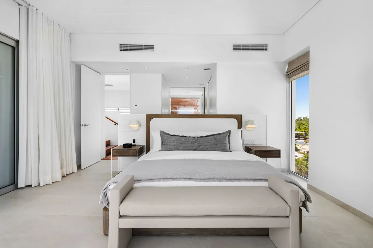 White bedroom with king bed and bench at Beach Enclave.