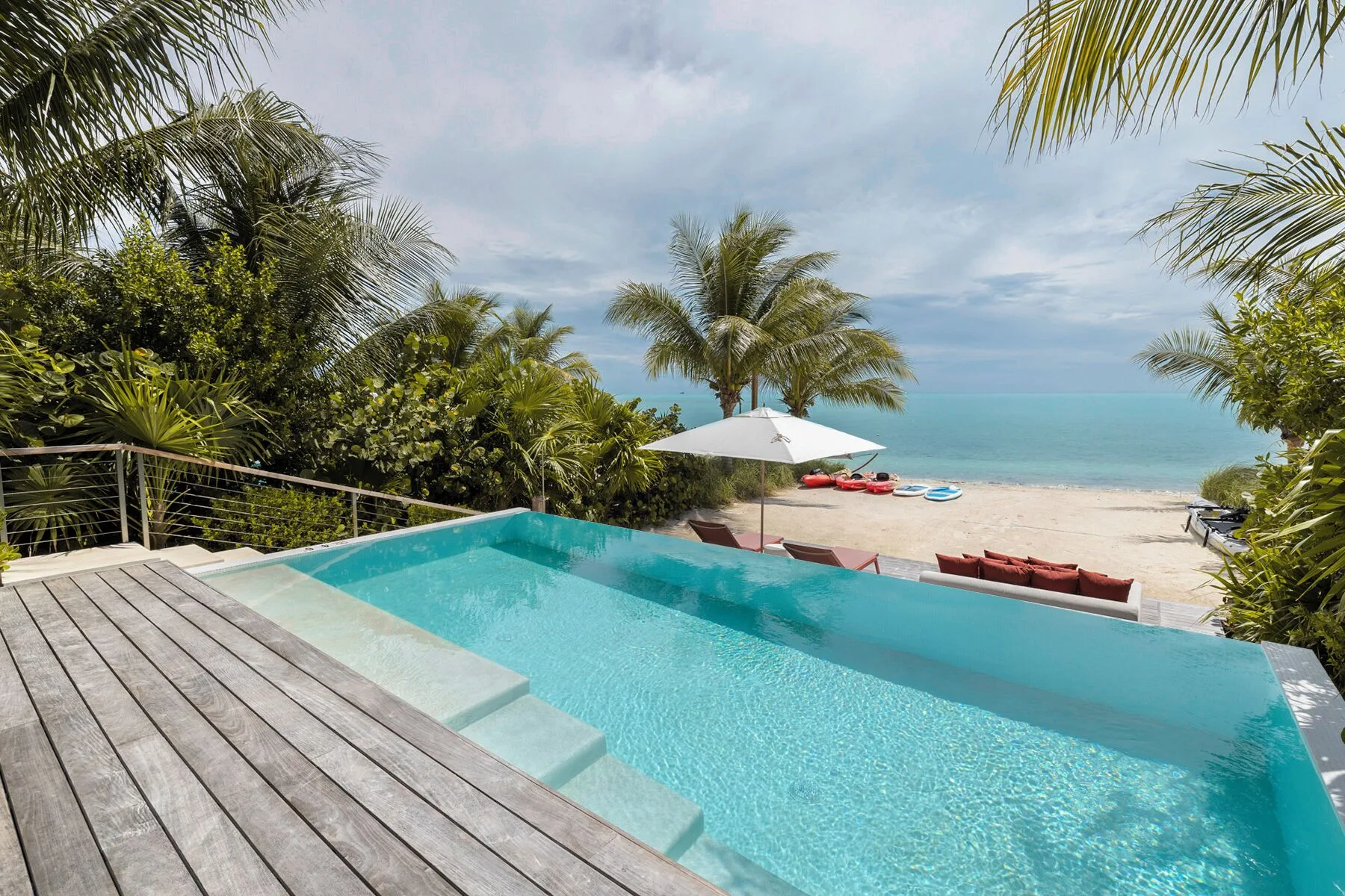 Beachfront infinity pool at Beach Enclave with palm trees, sand and turquoise water beyond.
