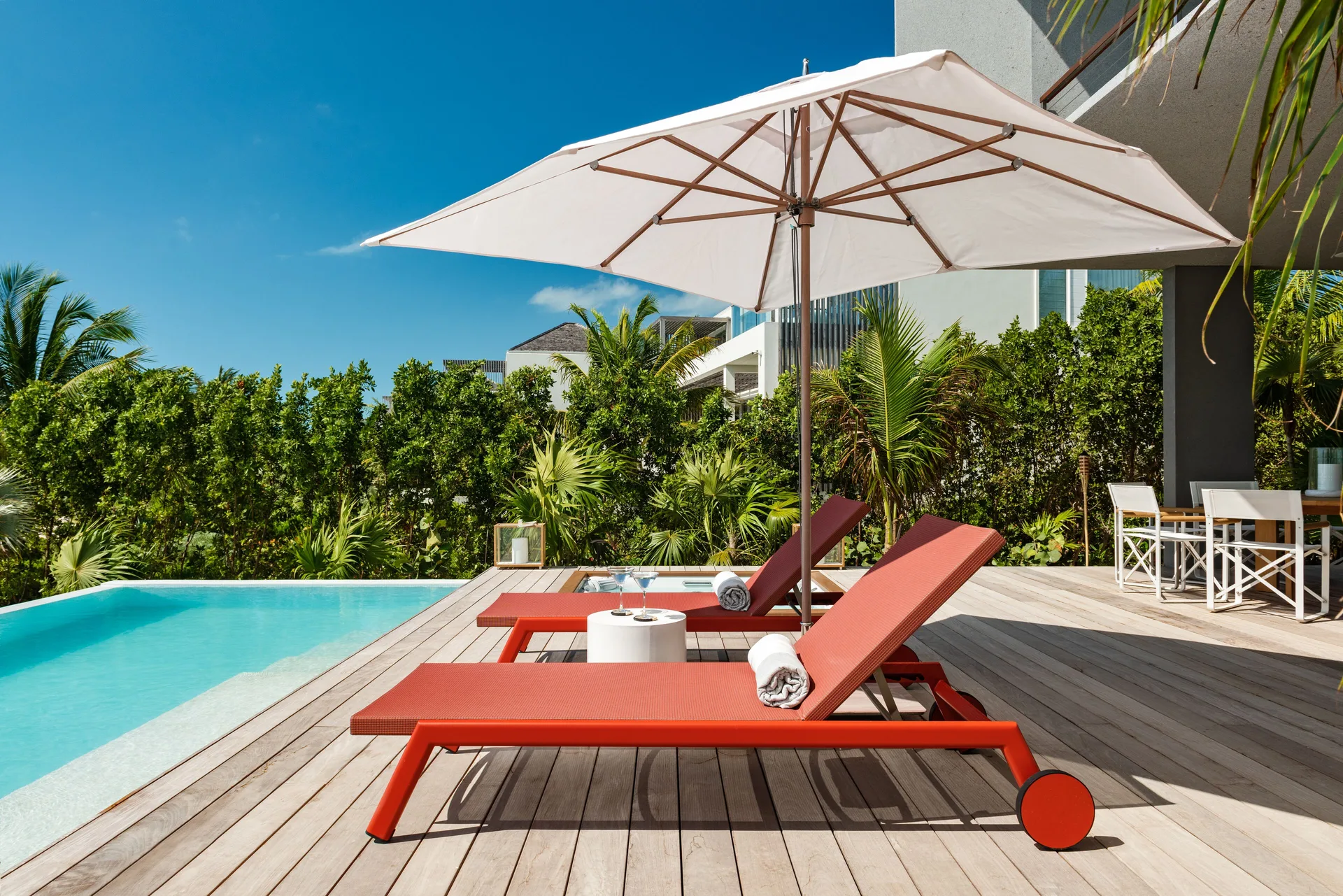 Pool deck at Beach Enclave with red loungers, white umbrella and tropical landscaping.