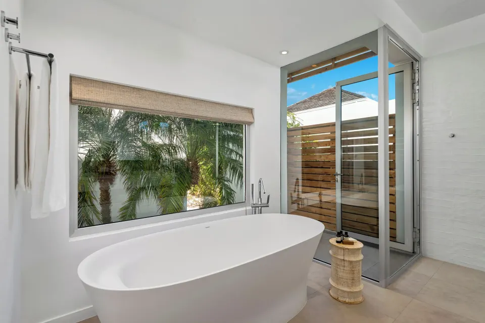 Bathroom at Beach Enclave with freestanding tub, garden window and glass shower door.