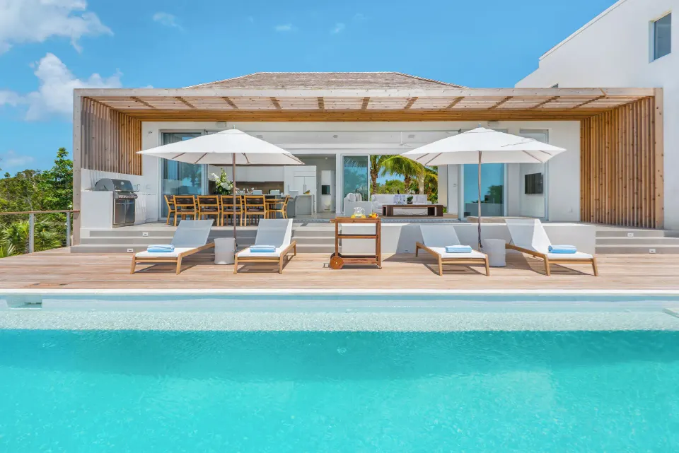 Pool terrace at Beach Enclave with loungers, umbrellas, outdoor dining and the villa behind.