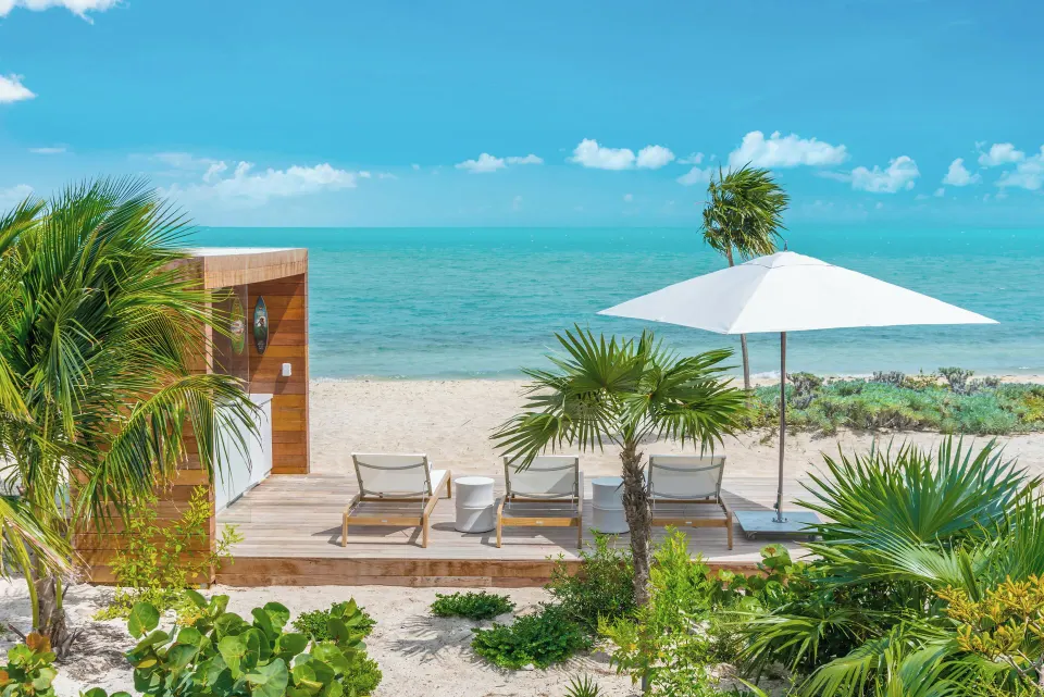 Beach deck with loungers, umbrella, palms, and ocean at Beach Enclave.