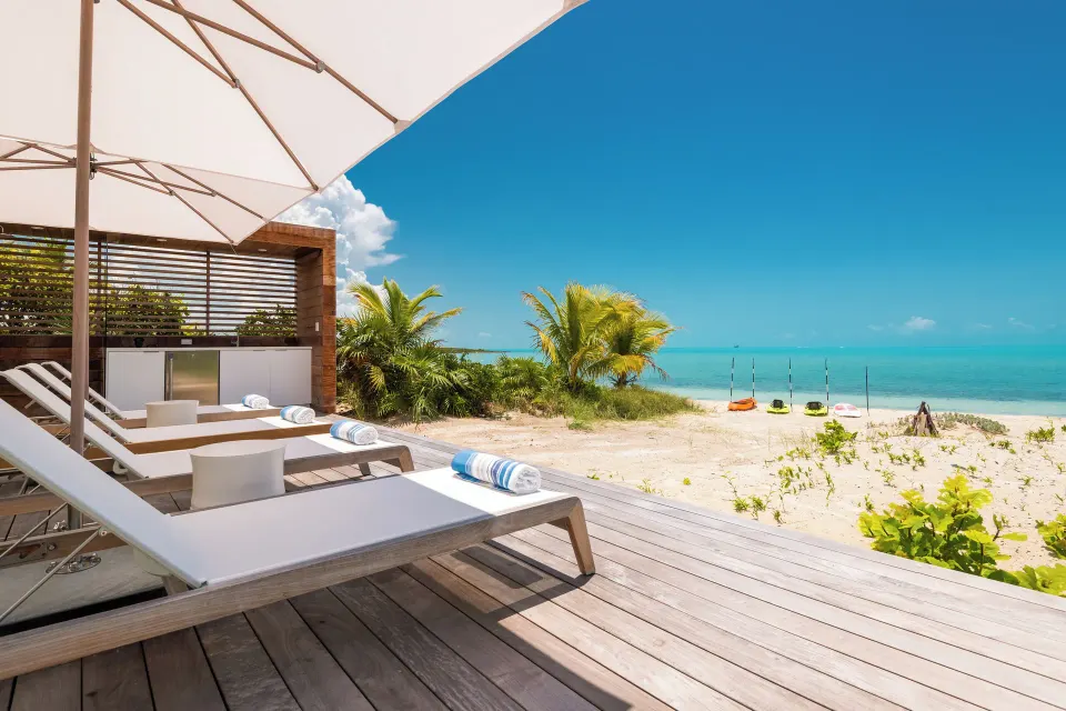 Beachfront deck with loungers, umbrellas, and turquoise sea at Beach Enclave.