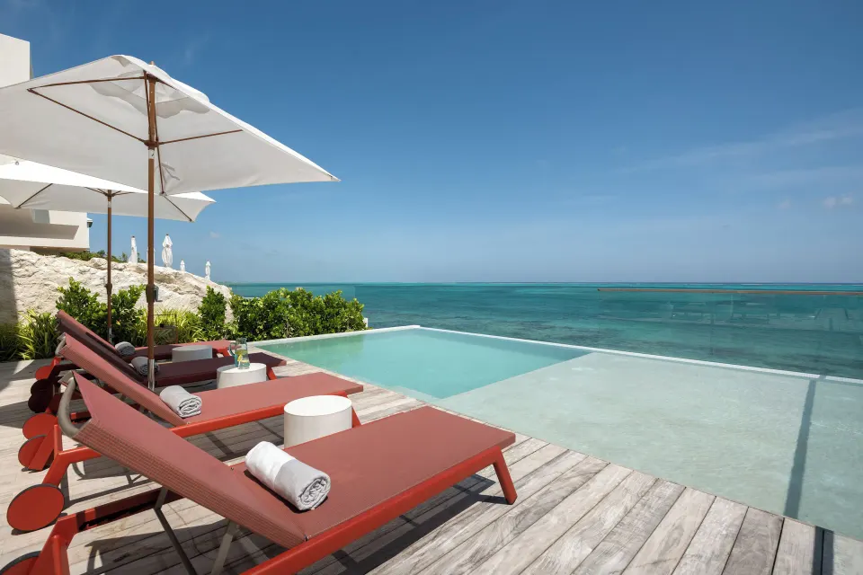 Pool terrace with red loungers, white umbrellas and ocean view at Beach Enclave.