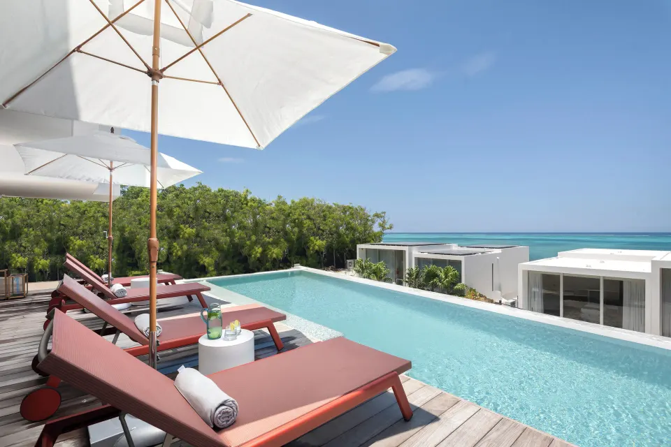 Private pool deck with loungers, umbrellas, and ocean view at Beach Enclave.