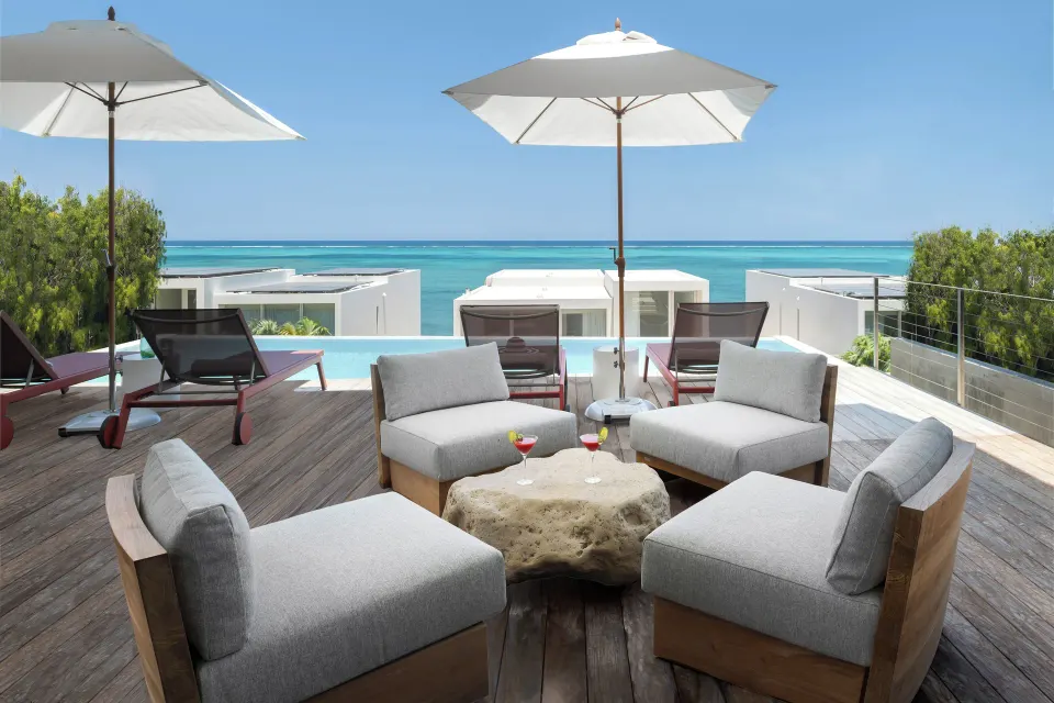 Ocean-view terrace seating at Beach Enclave with loungers, umbrellas, and turquoise water beyond.