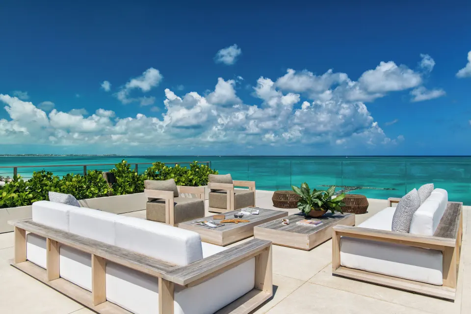 Oceanfront terrace seating at Beach Enclave with sofas, armchairs, tables and turquoise water beyond.