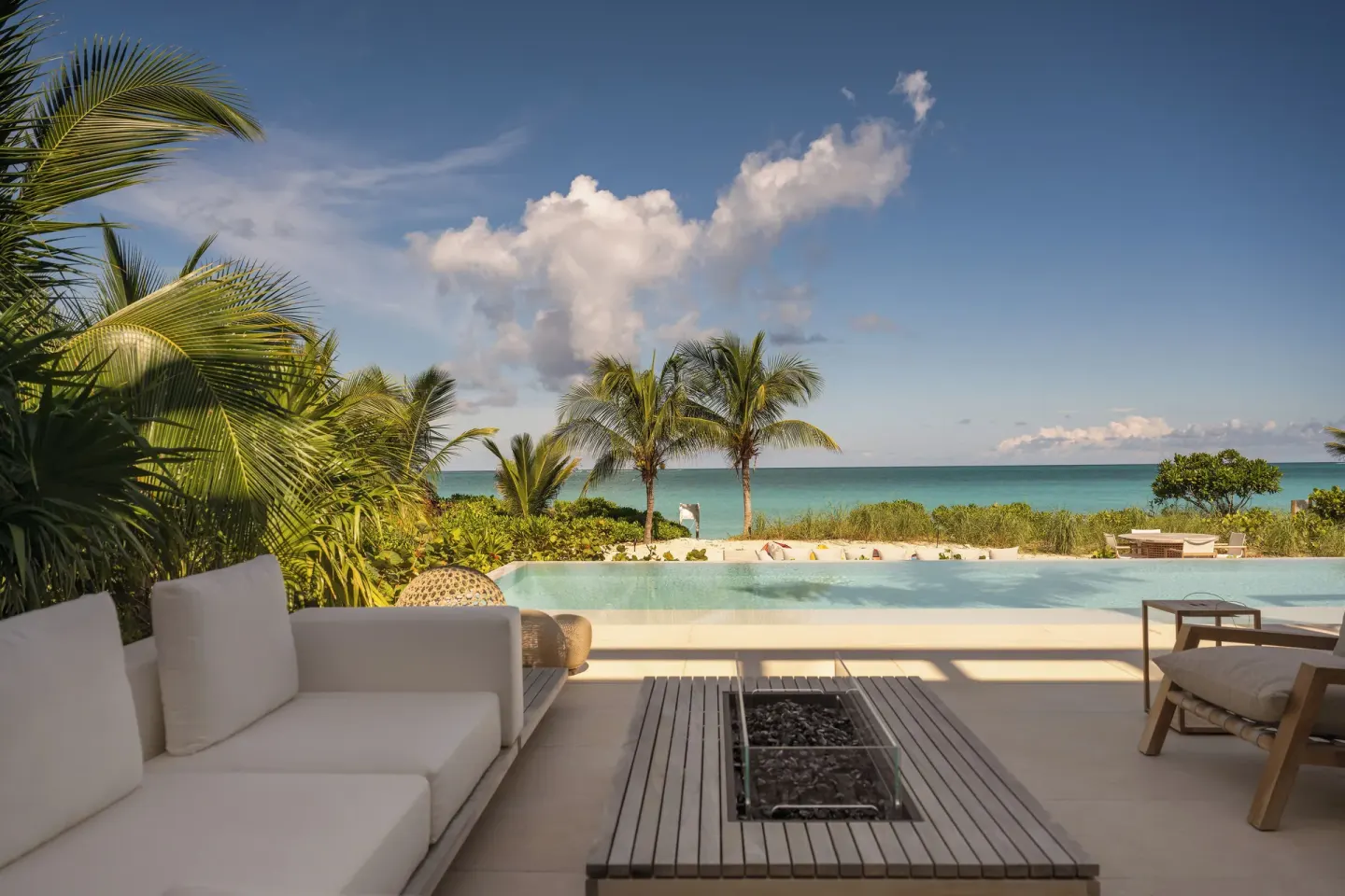 Poolside patio at Beach Enclave with cushioned seating, fire table, palms and ocean view.