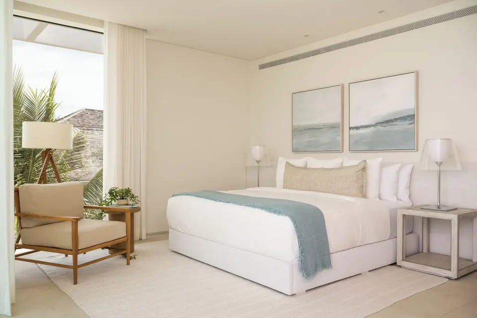 Bedroom with a large bed, blue throw, artwork and armchair at Beach Enclave.