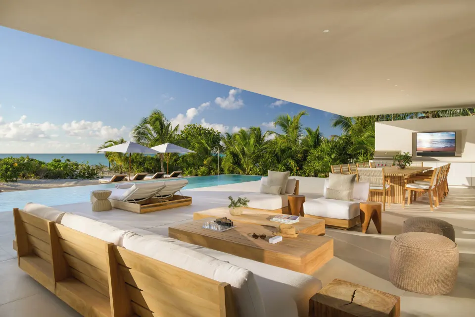 Covered outdoor living terrace with sofas, dining table, pool and ocean at Beach Enclave.