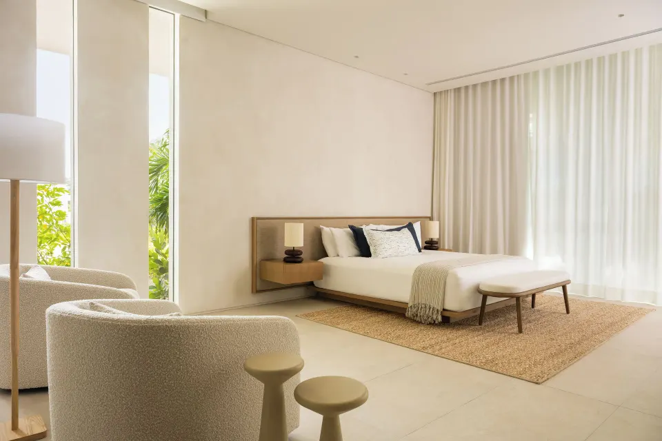 Minimal bedroom with a large bed, bench, lounge chairs and sheer curtains at Beach Enclave.