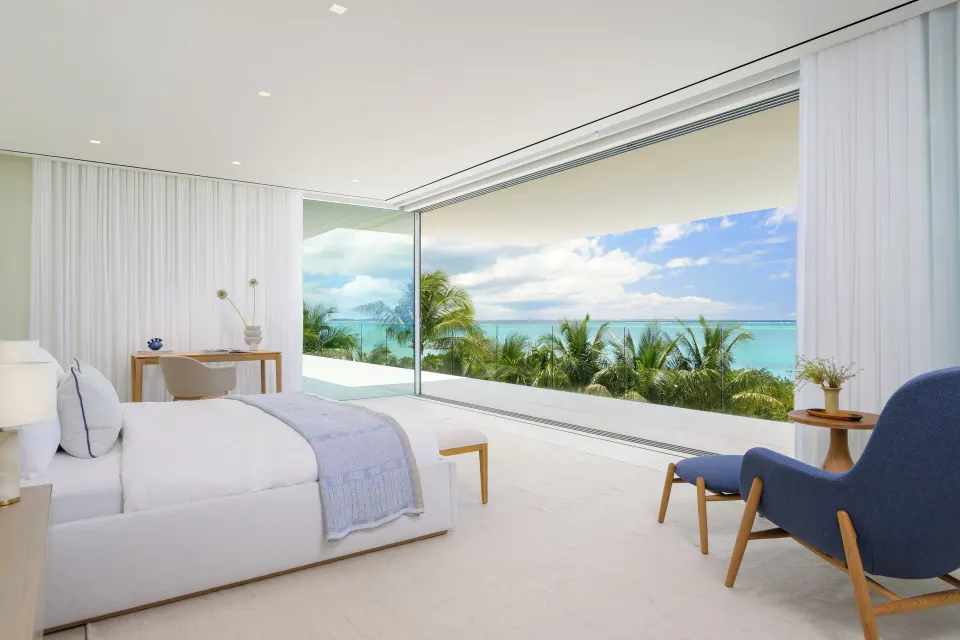 Oceanfront bedroom with a large bed, desk, blue chair and open glass wall at Beach Enclave.