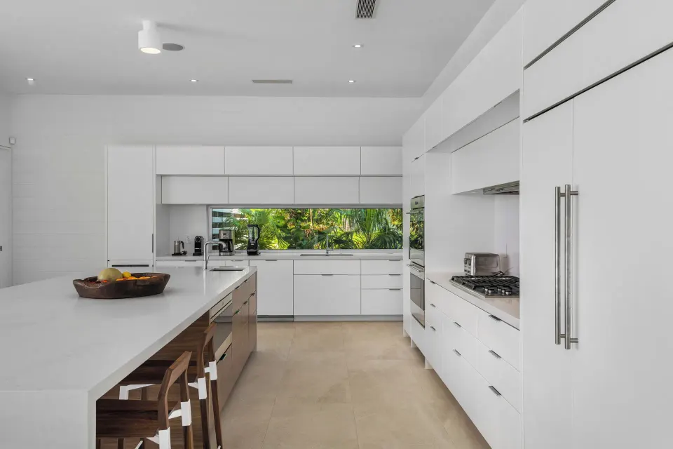 White villa kitchen with island seating and garden-view window at Beach Enclave.