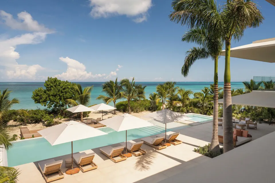 Oceanfront pool terrace with loungers, umbrellas, and palm trees at Beach Enclave.