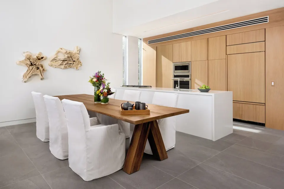 Dining table and kitchen with wood cabinetry in a beach house at Beach Enclave.