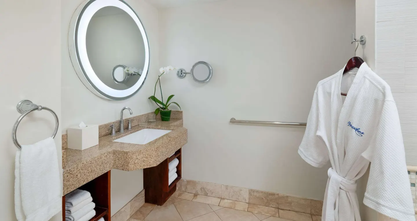 Bathroom vanity with robe, towels, and round lighted mirror at Beaches Negril Resort.