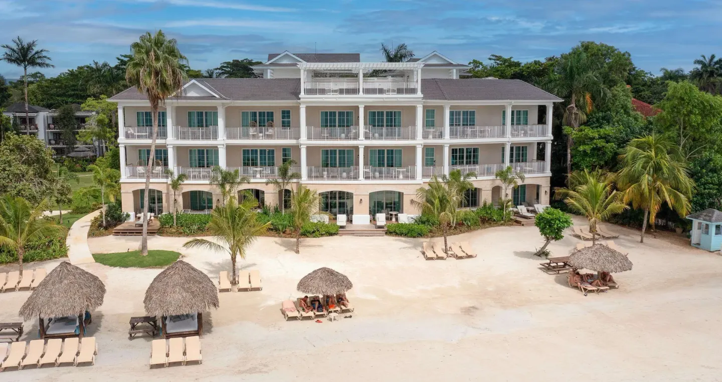 Beachfront resort building with balconies and palapa shade huts at Beaches Negril Resort.