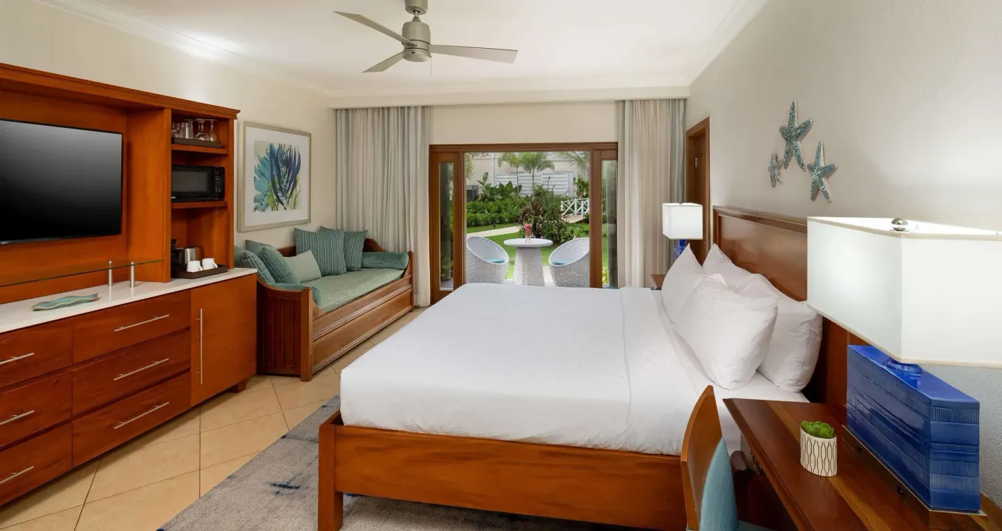 King bed guest room with patio doors and garden seating at Beaches Negril Resort.