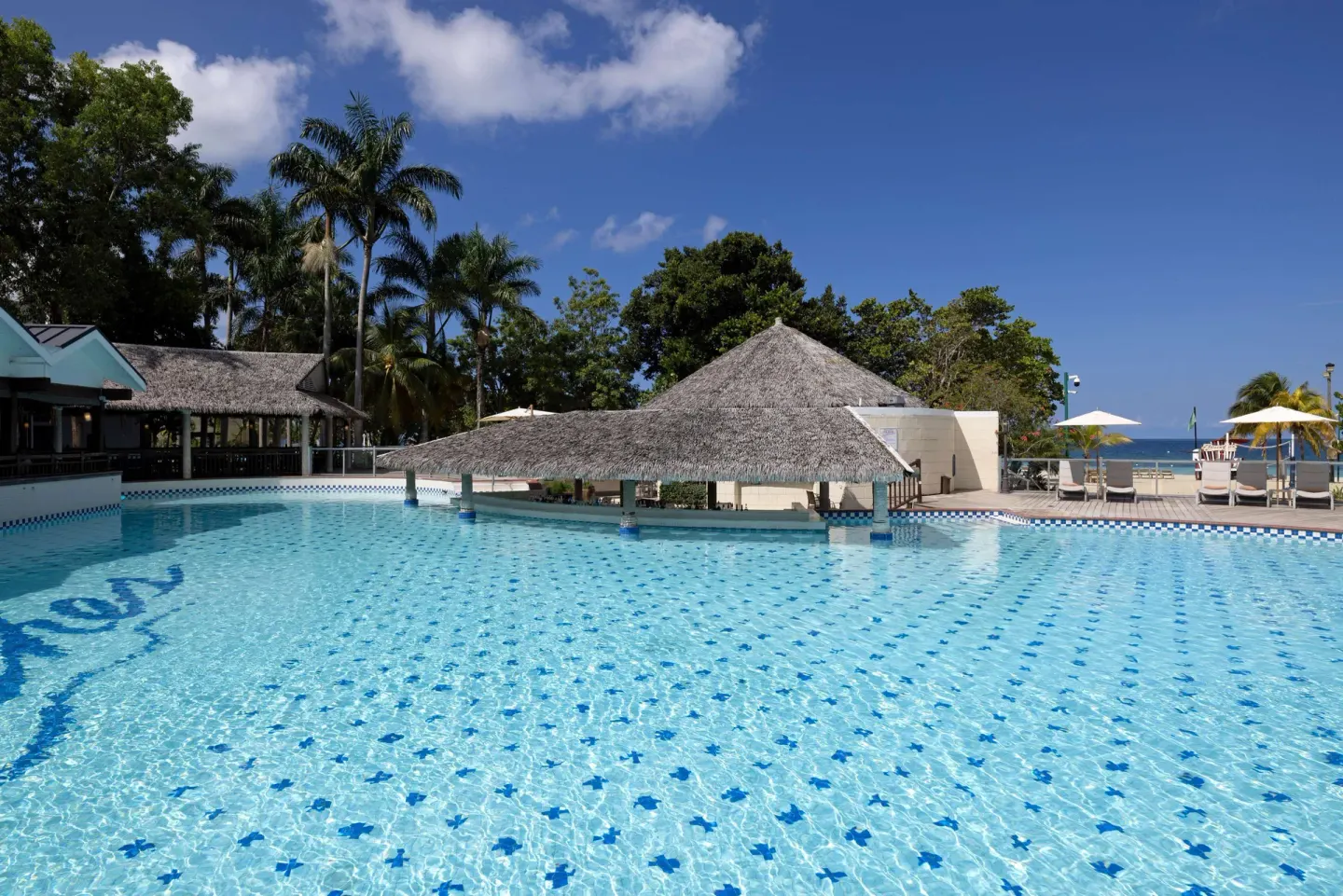 Pool with thatched shade structures and ocean glimpses at Beaches Negril Resort.