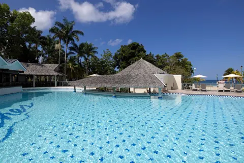 Pool with thatched shade structures and ocean glimpses at Beaches Negril Resort.