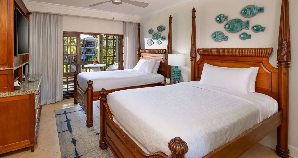 Two-bed guest room at Beaches Negril Resort with wood poster beds and balcony doors.