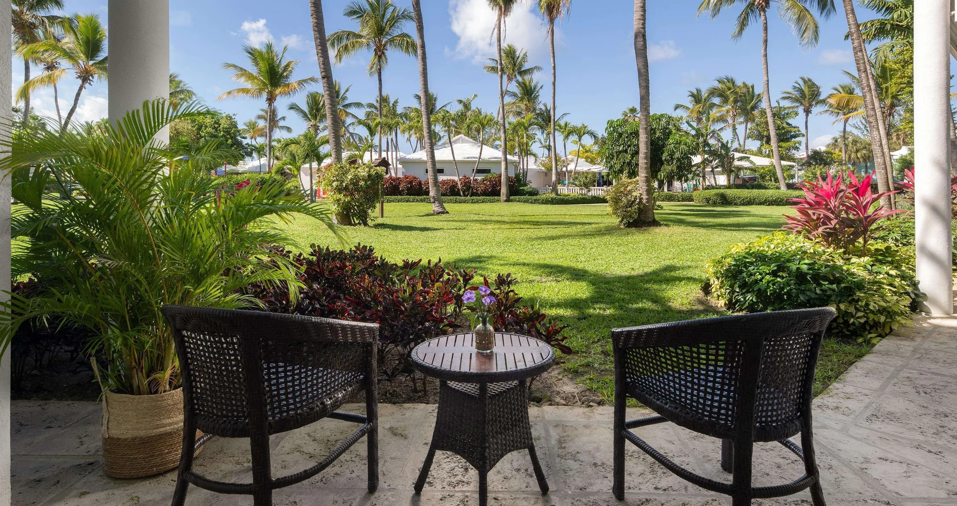 Garden patio at Beaches Turks & Caicos with two chairs, a small table, palms and manicured lawns.