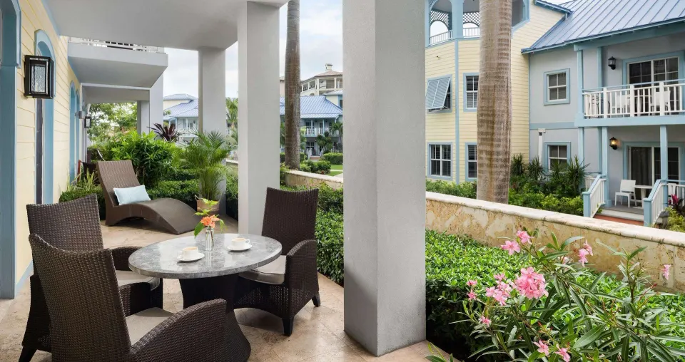 Garden-level patio at Beaches Turks & Caicos with wicker chairs, table, lounge chair and tropical landscaping.
