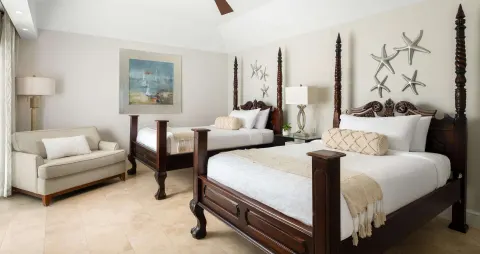 Second bedroom in a luxury suite at Beaches Turks & Caicos with two four-poster beds and a sofa.