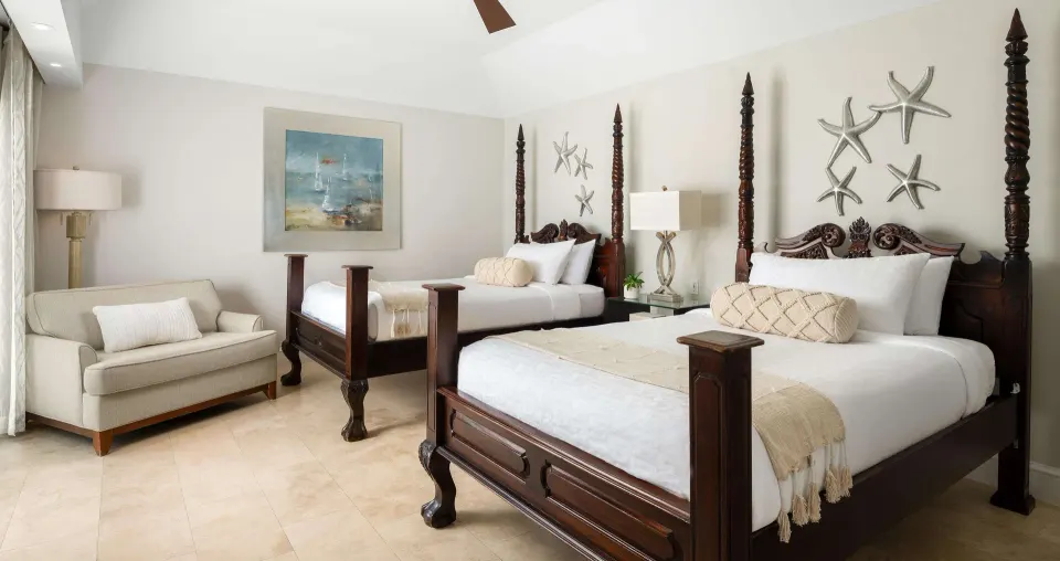Second bedroom in a luxury suite at Beaches Turks & Caicos with two four-poster beds and a sofa.