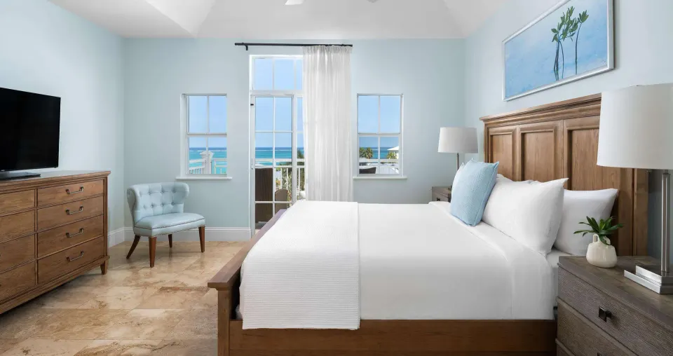 Ocean-view suite bedroom with white bed and balcony door at Beaches Turks & Caicos.